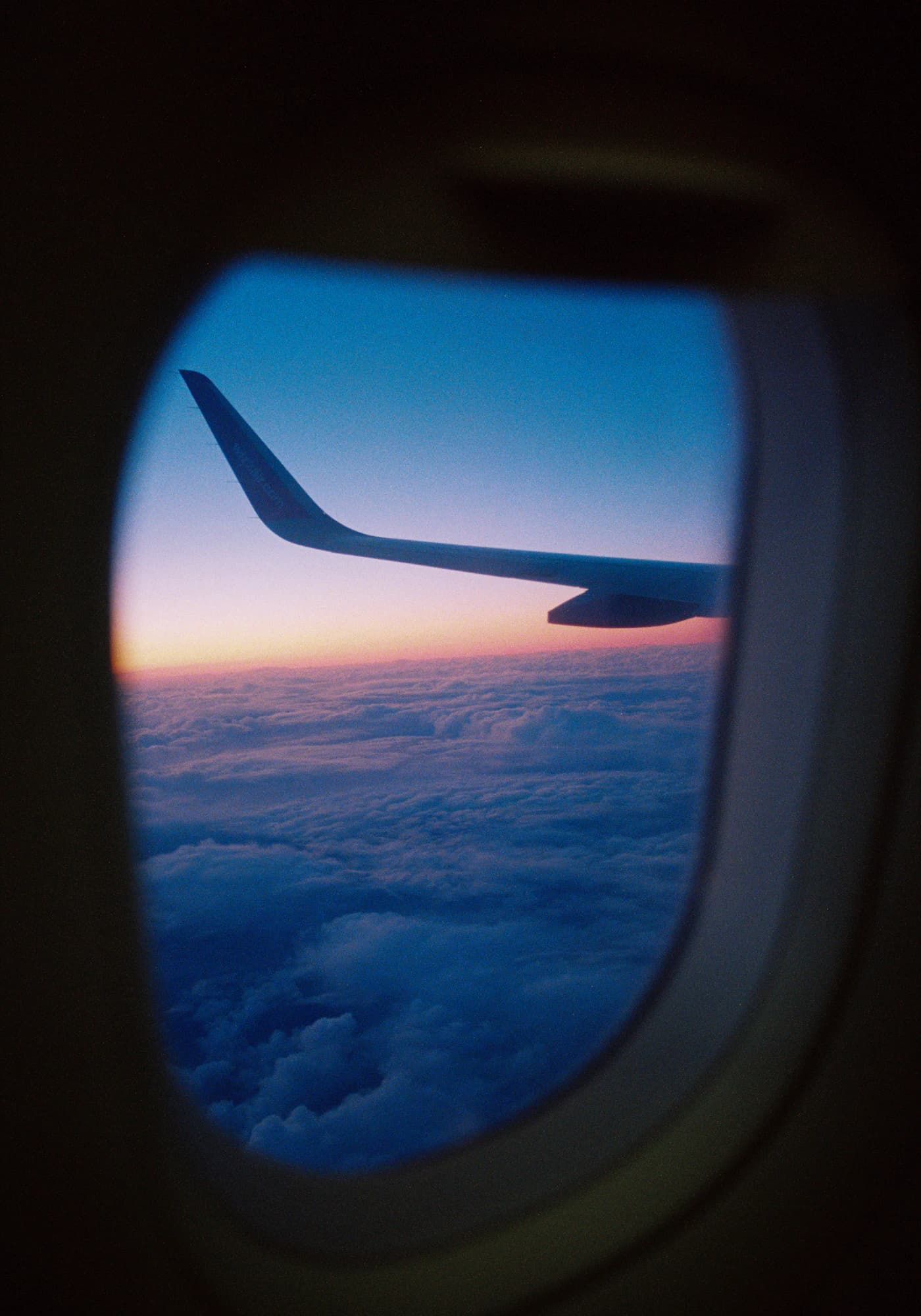 Plane wing above a sea of clouds, seen through a window seat at sunset