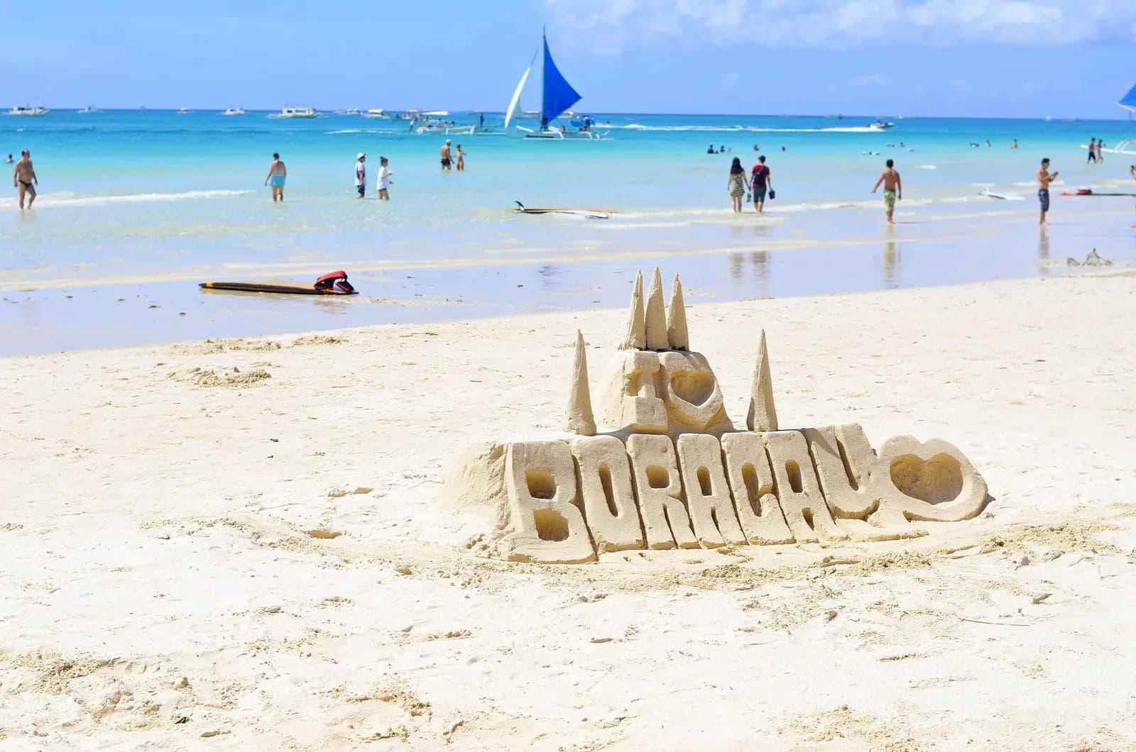 People walking the white sand shoreline of Boracay beach beside turquoise water